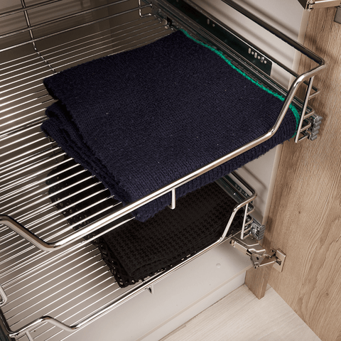 Pull-out chrome wire basket featuring neatly organized towels in a kitchen cabinet by KitchenLibrary.