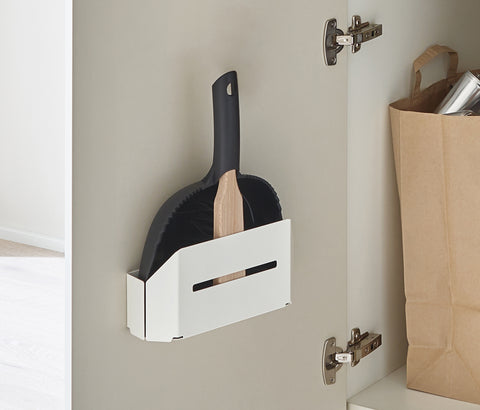 Peka white dustpan and brush holder mounted on a cupboard door, holding a dustpan and brush