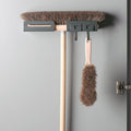 Peka Libell anthracite broom holder mounted on a cupboard door, holding a broom and hand brush