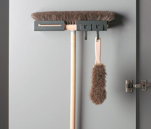 Peka Libell anthracite broom holder mounted on a cupboard door, holding a broom and hand brush