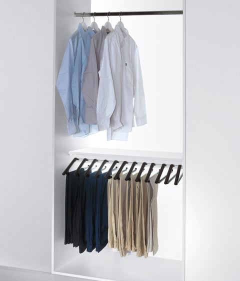 Peka Lina anthracite pull-out trouser rack in a white wardrobe, holding trousers on individual hangers below a shelf of shirts
