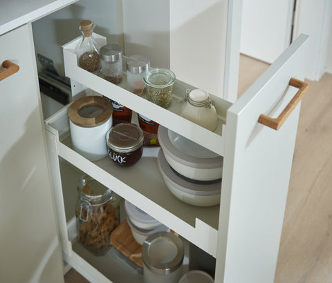 Peka Pinello Cargo white base unit pull-out with oak handle storing jars and bowls on tiered shelves in a white kitchen