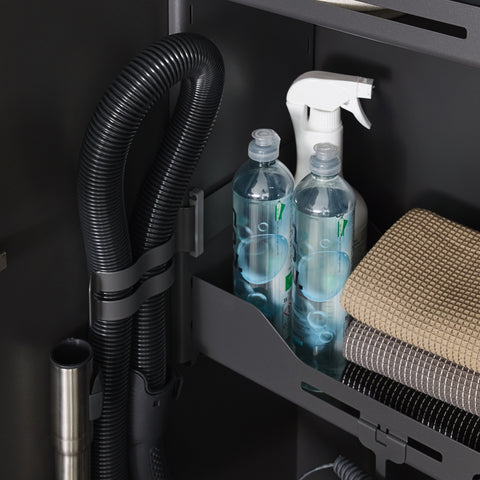 Close-up of Peka Sesam Standard anthracite shelf with cleaning bottles, folded cloths and a vacuum hose holder